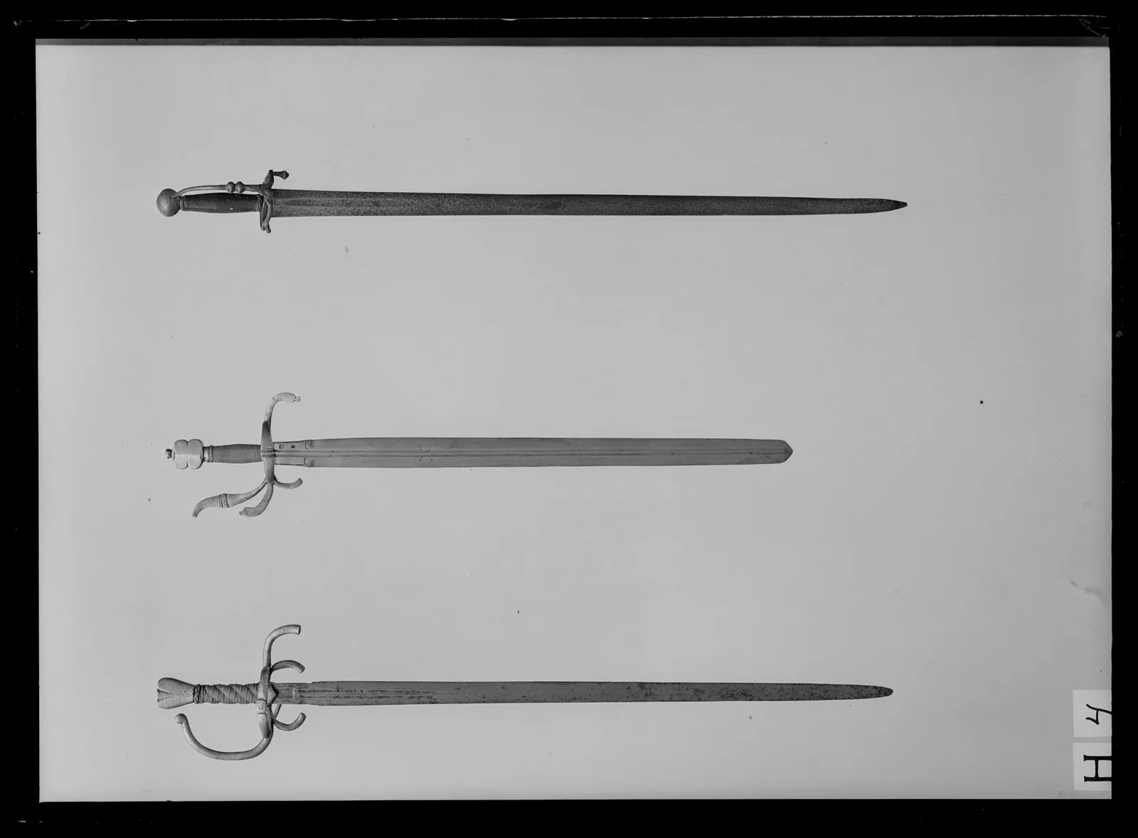 Värja, fäste och klinga ej samhörande, fäste: Tyskland ca 1575-1600, klinga: Tyskland 1600-talets första hälft. # #3# Fäste av stål, slätt, på mitten av handbygel och kryssbygel en tvär-ställd räfflad bård. Knapp platt, kantkonturen med inskuret mittparti, Ut- och insidorna fasade från en vertikal m